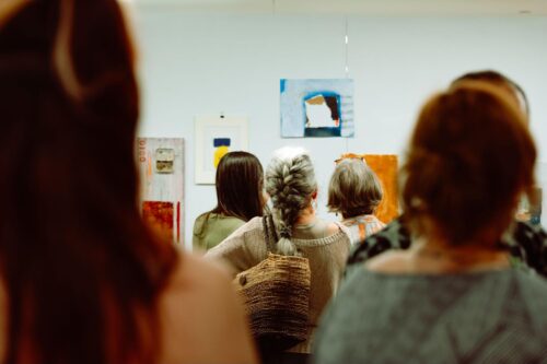 A group of students in the MFA in Visual Art program at VCFA look at various pieces of artwork hanging on a gallery wall.