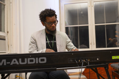 A VCFA MFA in Music Composition student plays the keyboard in a brightly-lit classroom.