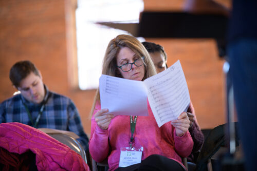 A VCFA MFA in Music Composition student examines a piece of sheet music. In the background, other students look on as well.