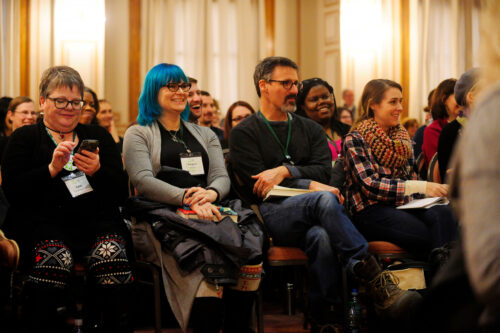 Smiling VCFA students listen to a lecture on how to write a picture book.