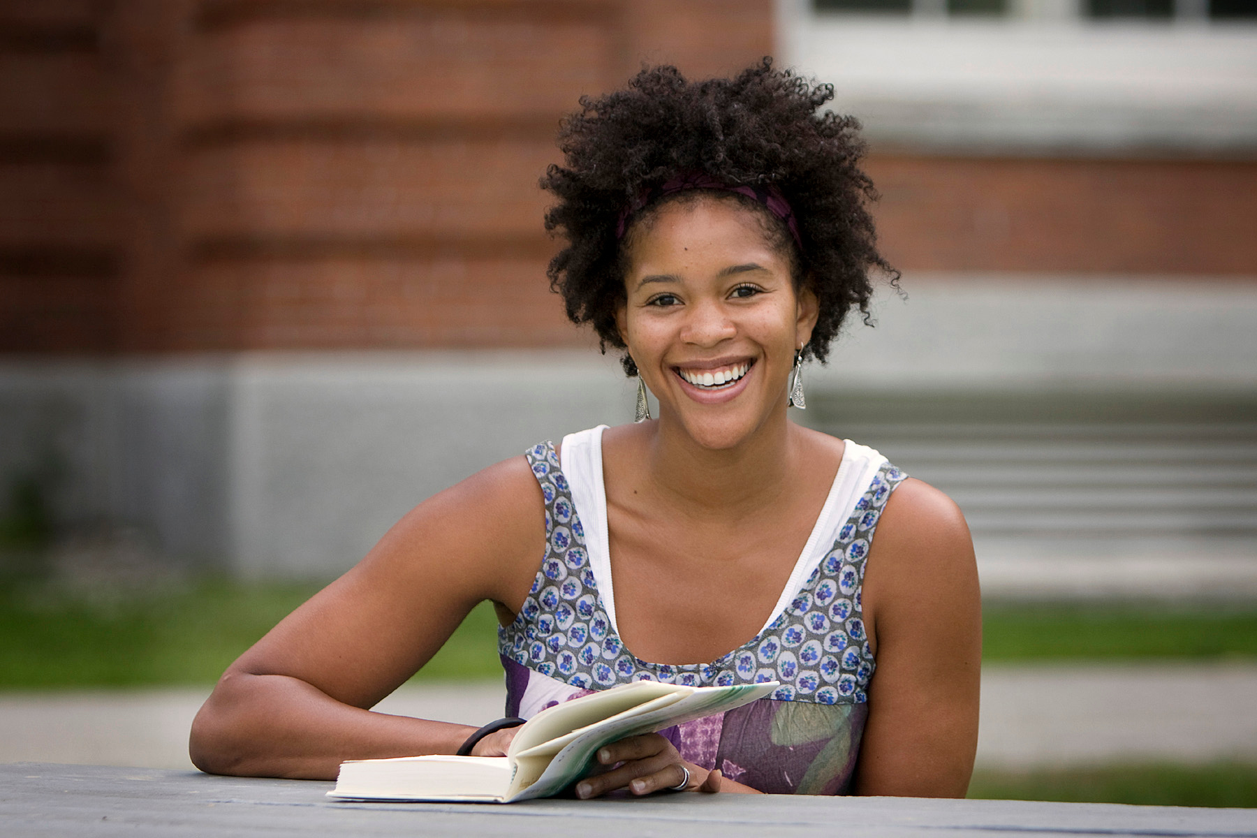 Smiling VCFA student reads a book about writing prompts on campus.