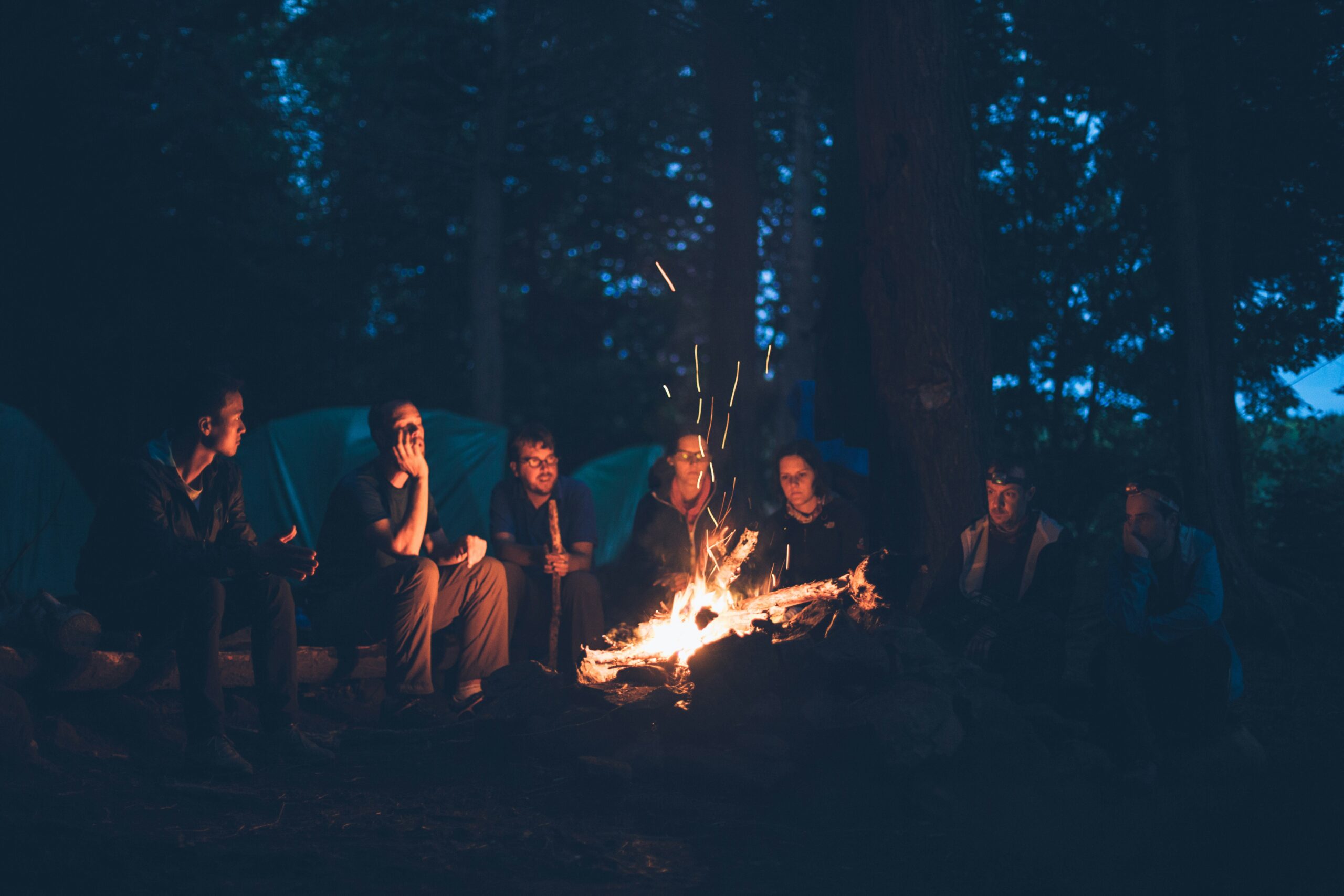 People sit around a campfire telling scary stories and talking about horror writing prompts.