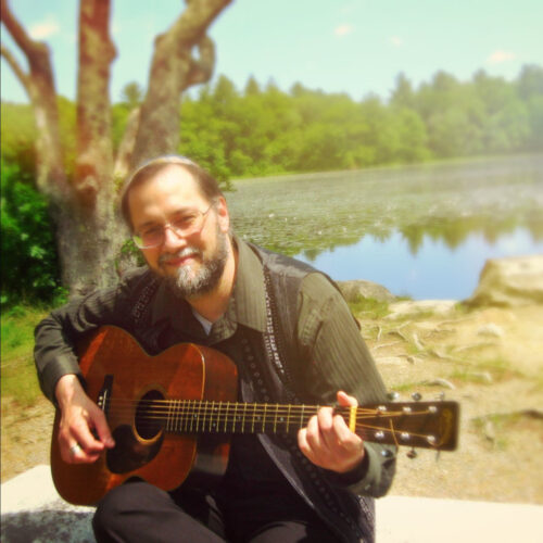 Daniel Gil sitting by a lake holding his guitar